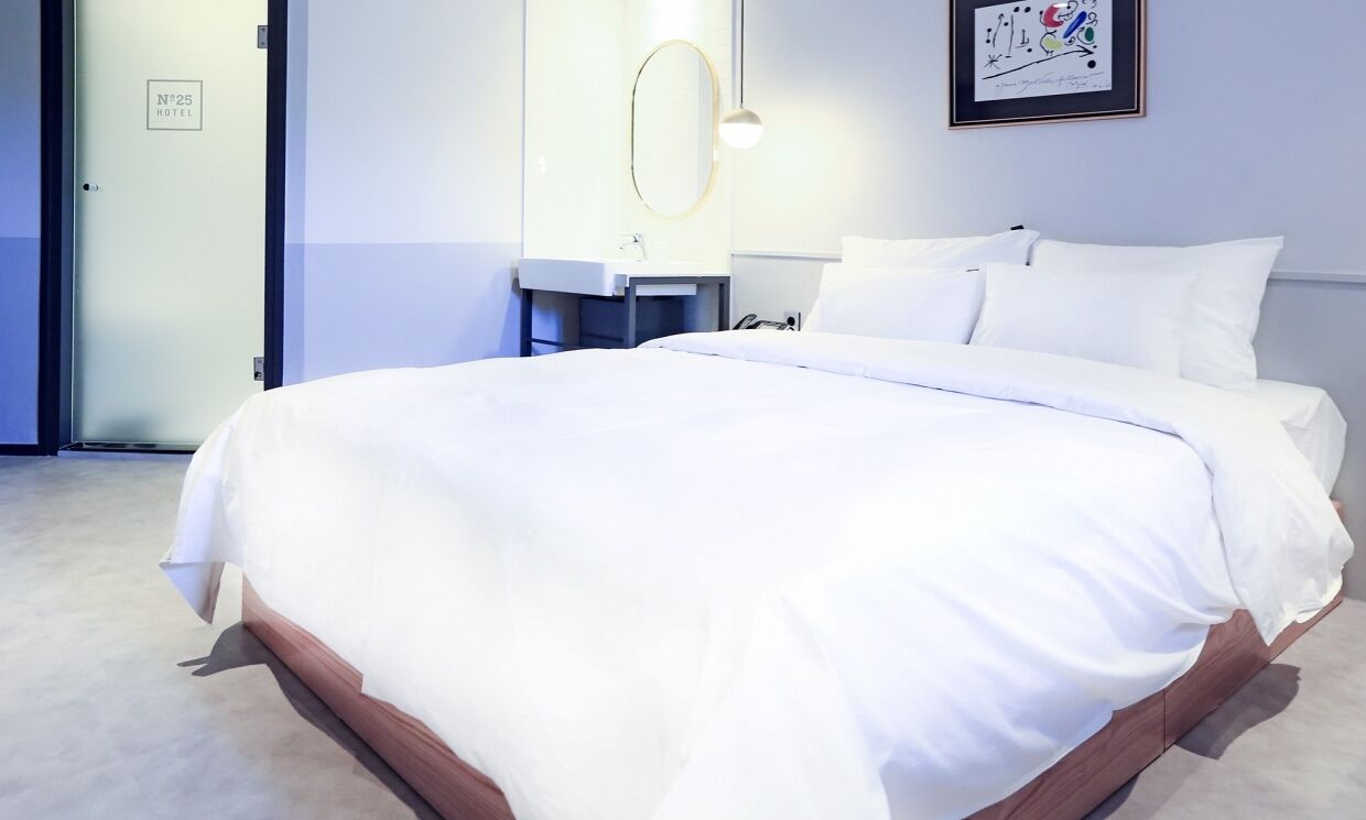 A hotel room with a large bed, a bedside table, a mirror, and a framed picture on the wall.