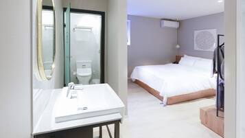 A modern hotel room with a large bed, a bathroom with a toilet and sink, and a mirror.