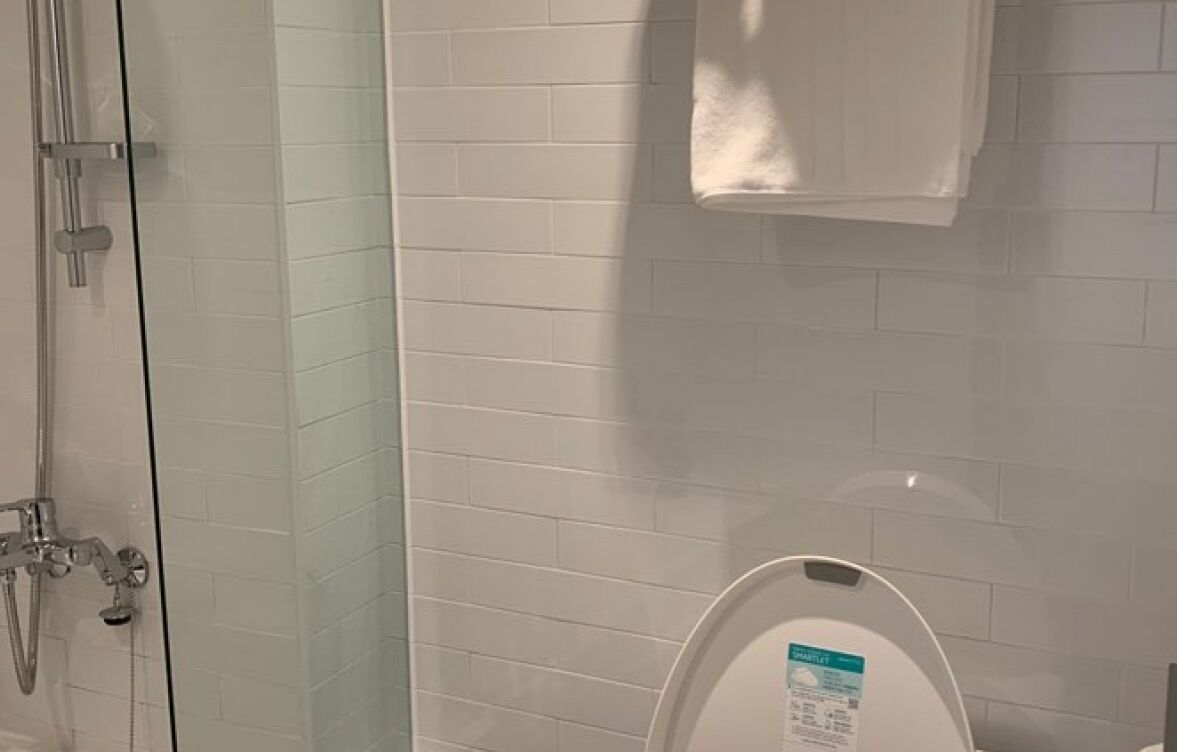 A bathroom with white tiled walls, a glass shower enclosure, and a white toilet with a visible label.