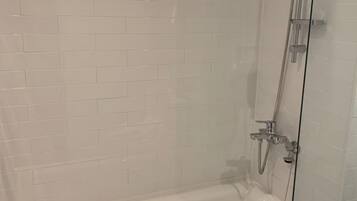 Un área de ducha con paredes de azulejos blancos y un cabezal de ducha visible, todo ello envuelto en vidrio.