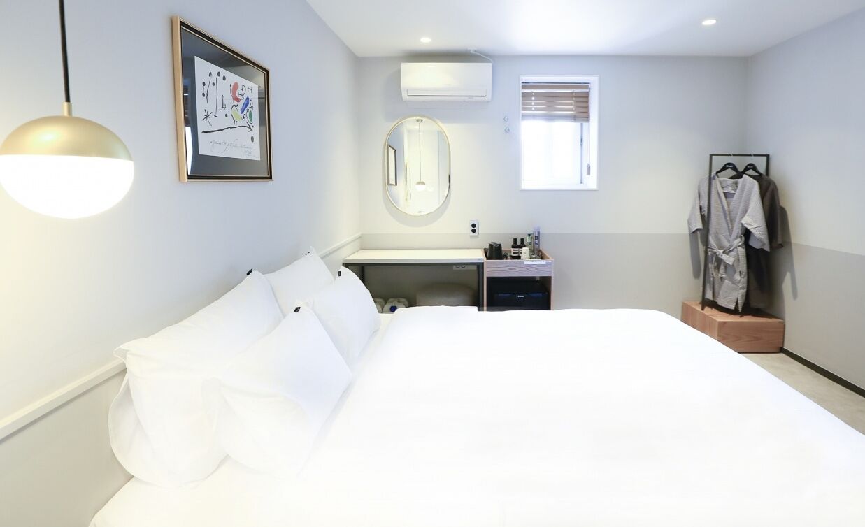 Habitación de hotel con una cama grande, una mesita de noche, un espejo, una ventana y un perchero para bata.