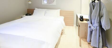 Una cama bien hecha con sábanas blancas, un cabecero de madera, una mesita de noche con un teléfono y una lámpara, y una bata colgada en un perchero.
