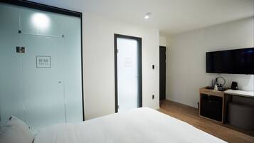 A hotel room with a bed, a TV, a desk with a coffee machine, and a wardrobe.
