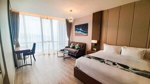 A hotel room with a large bed, a desk with a chair, a sofa, and a painting on the wall. - Cala Coastline Panorama (Nha Trang)