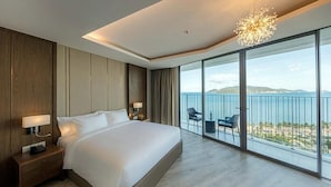 A modern hotel room with a large bed, a nightstand, a desk, and a balcony with a view of the sea. - Cala Coastline Panorama (Nha Trang)