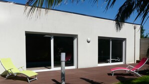 A modern building with large sliding glass doors, two lounge chairs, and a concrete planter. - The bay house with heated indoor pool (Saint-Jean-du-Doigt)