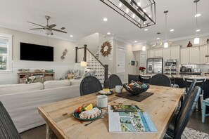 A modern kitchen with stainless steel appliances, a dining area with a wooden table and chairs, and a living room with a sofa and a TV.