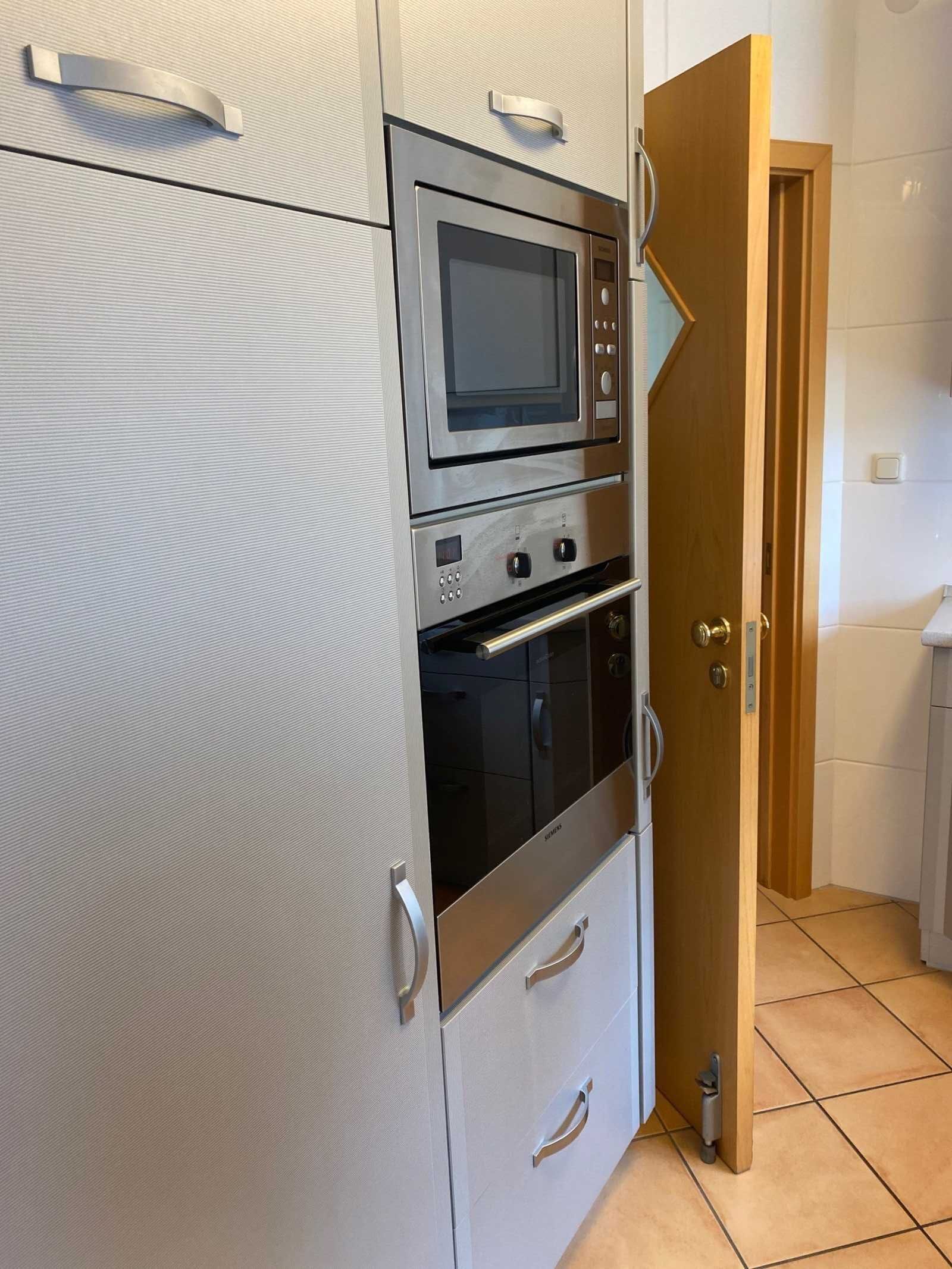 Eine kompakte Küche mit eingebauter Mikrowelle und Backofen, einer Holztür und einem Fliesenboden.