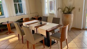 A dining area with a table set for six, surrounded by chairs, a sofa, and a large potted plant. - Luxuröses Apartment im Erdgeschoß - Weserlounge Apartments (Hessisch Oldendorf)
