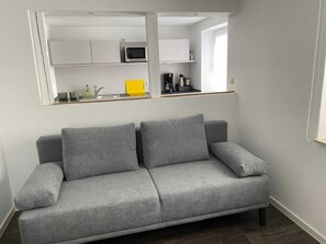 Un canapé gris dans un salon moderne, avec une cuisine située à l’étage supérieur, comprenant un four à micro-ondes et une machine à café.