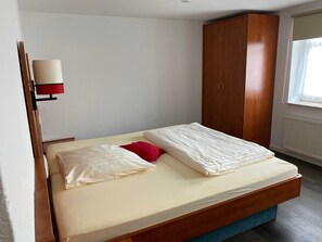 Un lit simple avec un cadre en bois, un matelas bleu, un oreiller rouge et une tête de lit blanche.