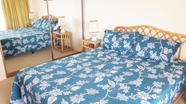 A room with two beds, each with floral-patterned bedding and wooden headboards. There are bedside tables with lamps and a mirror on the wall. - Sandbar Unit 302 (Forster)