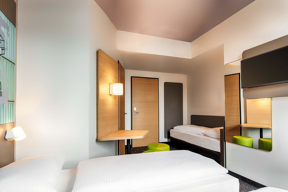 A modern hotel room with a bed, bedside tables, a mirror, and a wall-mounted shelf.