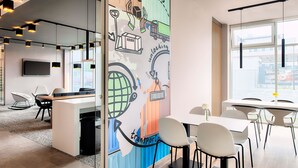 A modern office space with a large desk, chairs, a television, and a mural depicting global delivery and transportation. - B&B Hotel Stuttgart-Neckarhafen (Stuttgart)