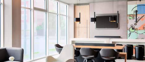 Un interior moderno con ventanas amplias, un televisor de pantalla plana y una zona de estar con mesas y sillas.