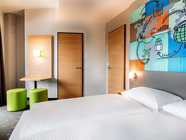 A hotel room with a bed, two green stools, a wooden wardrobe, and a wall with a colorful map and loading icon.