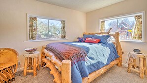 Una camera accogliente con un letto di legno, due finestre con tende, un tavolino e una sedia.
