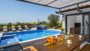 A poolside area with a wooden table set for breakfast, a small waterfall feature, and a view of the landscape. - Villa A.R.T. Viskovici (Koromačno)