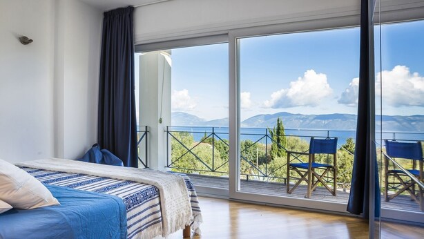 Ein Schlafzimmer mit einem großen Bett, einem Balkon mit Blick auf das Meer und die Berge sowie einem Tisch mit Stühlen.