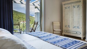 Ein Schlafzimmer mit Bett, einem Holzstuhl, einem Kleiderschrank und einem Balkon mit Blick auf Grünflächen.