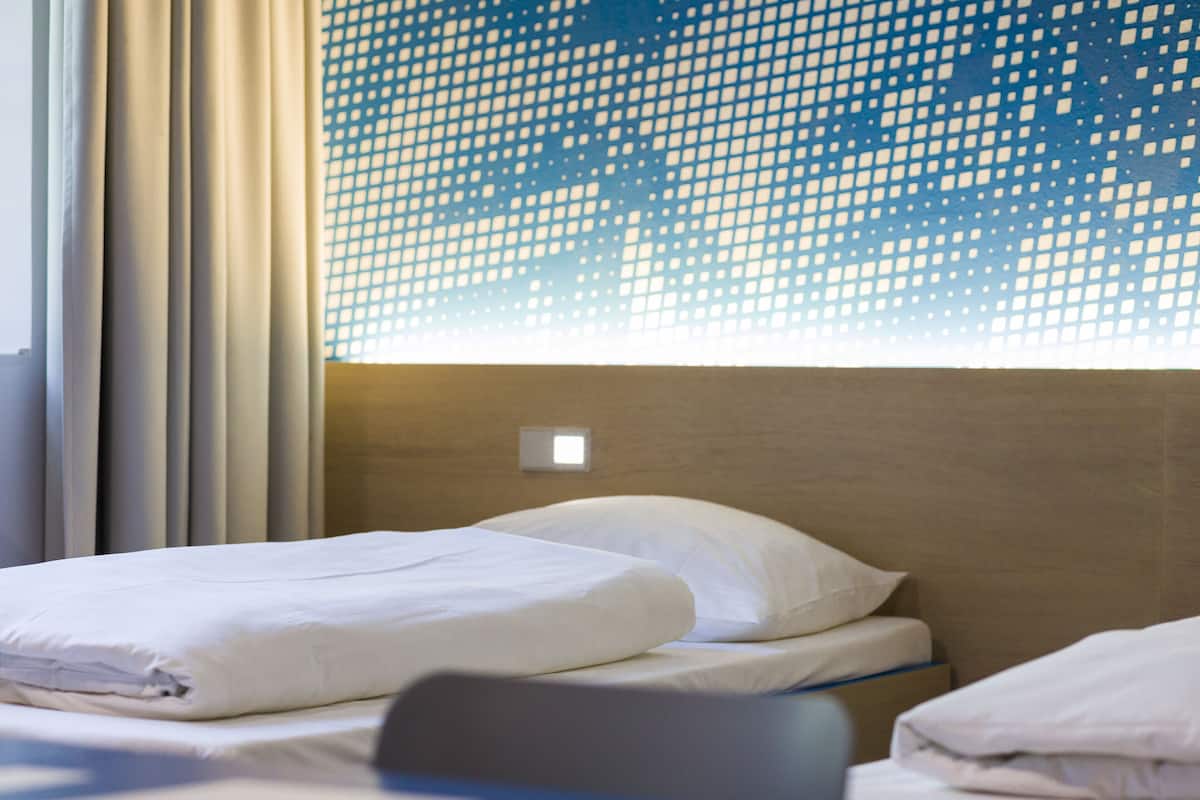 A hotel room with a bed, curtains, and a window with a geometric pattern.