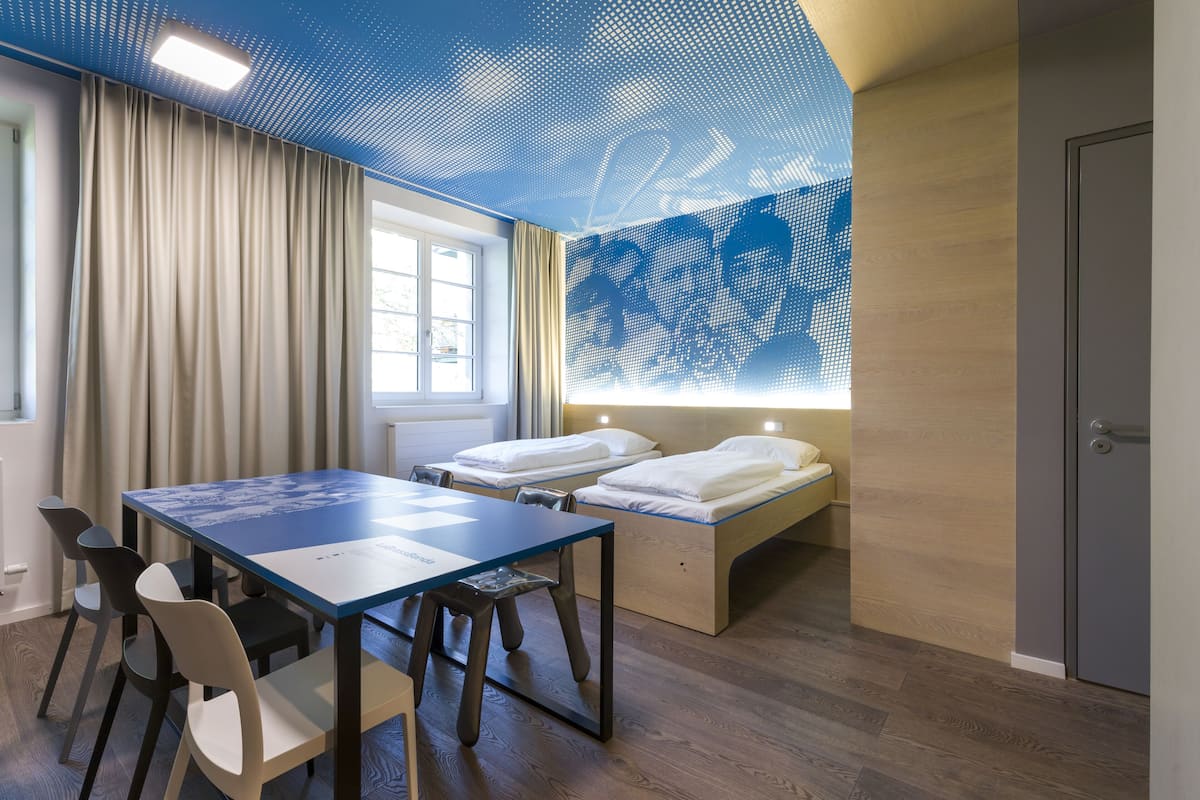 A modern room with a wooden floor, a blue table, and a bed with white bedding.