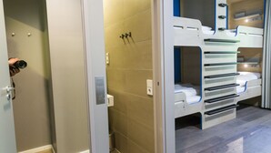 Uma casa de banho moderna com chuveiro, sanita e lavatório. Há beliches com compartimentos de arrumação.