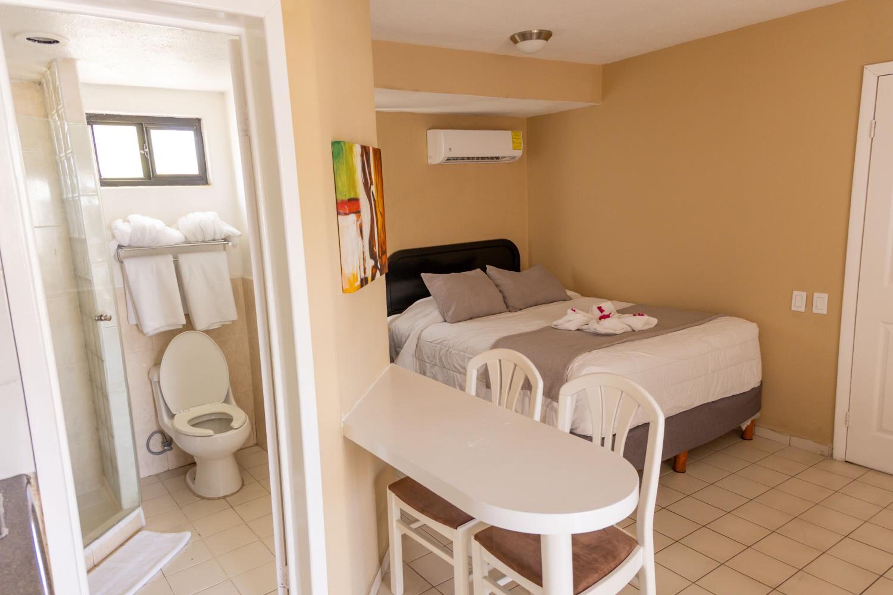 Ein kleines, sauberes Zimmer mit Bett, Nachttisch, Stuhl, Toilette und Dusche.