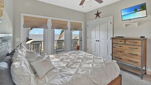 Una camera da letto con un letto, una ventola a soffitto, una TV, una cassettiera e vista sulla spiaggia.