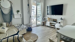 A modern living room with a sofa, a small round table, a TV, and a balcony with a view of buildings.