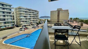 Ein Balkon mit Pool, Stühlen und Blick auf das Meer und Gebäude.