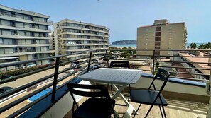 A balcony with a table and chairs, overlooking a parking area and buildings with balconies, under a clear sky.