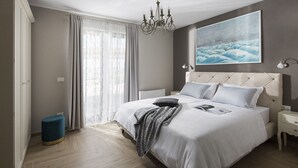 A modern bedroom with a large bed, a chandelier, a painting, and a view of the outdoors.