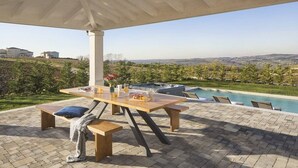 An outdoor patio with a table and benches, a pool, and a view of the landscape.