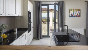 A modern kitchen with a black countertop, white cabinets, and a view to a patio with a table and chairs.
