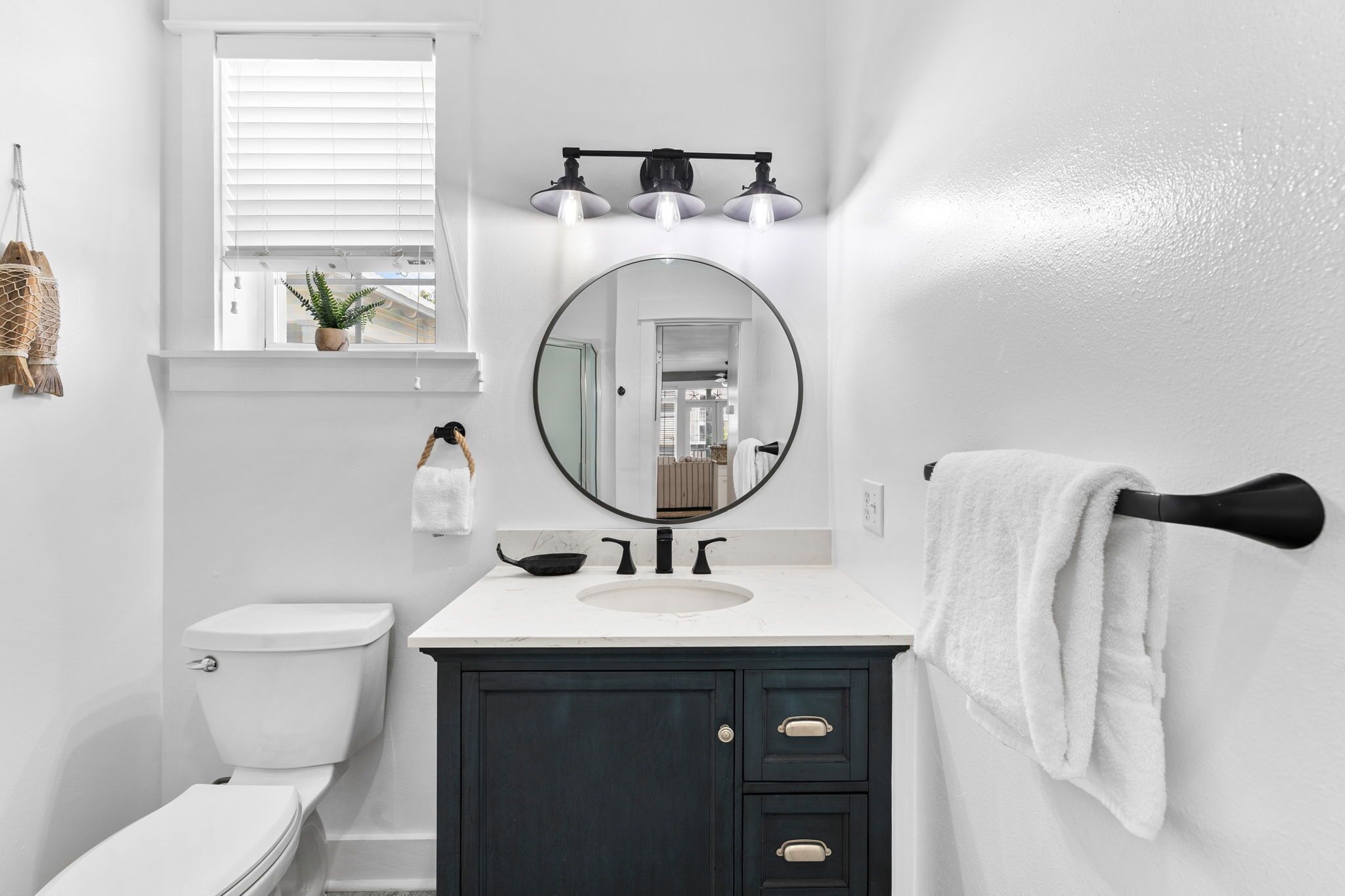 A bathroom with a white toilet, dark cabinets, a round mirror, and a towel rack.