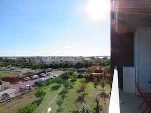 A balcony with a view of a parking lot, greenery, and distant buildings.