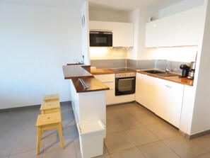 A compact kitchen with a microwave, oven, sink, and wooden stools.
