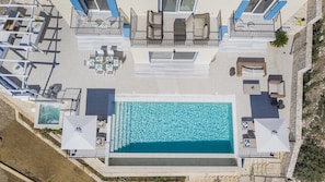 Une vue aérienne d’un hôtel doté d’une piscine centrale, de plusieurs espaces de détente en plein air et d’un mur en pierre.