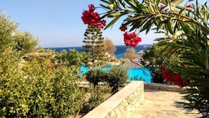 A stone pathway leading to a pool with a clear view of the sea and a building in the background. - New listing House with huge pool and private beach (Ornos)