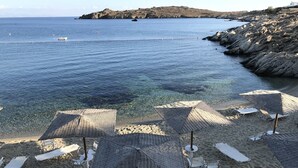 A beach with clear blue water, rocky coastline, and several beach umbrellas and lounge chairs. - New listing House with huge pool and private beach (Ornos)