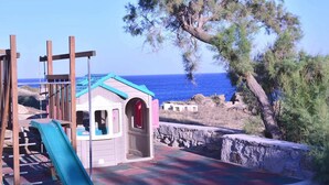A playground with a slide and climbing structure, set against a backdrop of the sea and trees. - New listing House with huge pool and private beach (Ornos)