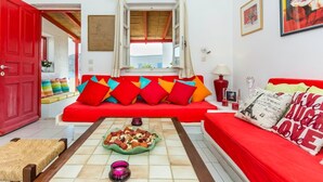 A living room with a red sofa, colorful cushions, a coffee table with snacks, and a red door. - New listing House with huge pool and private beach (Ornos)