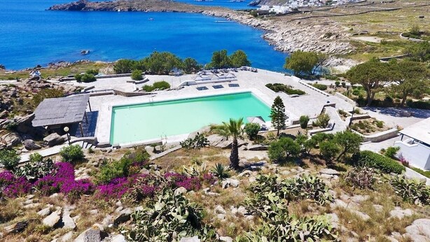 A pool area with a clear view of the sea, surrounded by rocky terrain and sparse vegetation. - New listing House with huge pool and private beach (Ornos)
