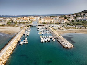 An aerial view of a marina with boats docked, a bridge connecting to the mainland, and surrounding residential buildings.