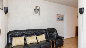 A black leather sofa with three cushions in a room with white textured walls, two framed pictures, and a wooden floor. - Apartment Milić  (Dubrovnik)
