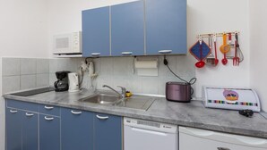 A kitchen with blue cabinets, a microwave, a toaster, and various utensils hanging on the wall. - Apartment Milić  (Dubrovnik)