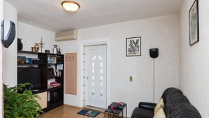 A living room with a black leather sofa, a small table with a red cup, a potted plant, a bookshelf, and a white door with glass panels. - Apartment Milić  (Dubrovnik)