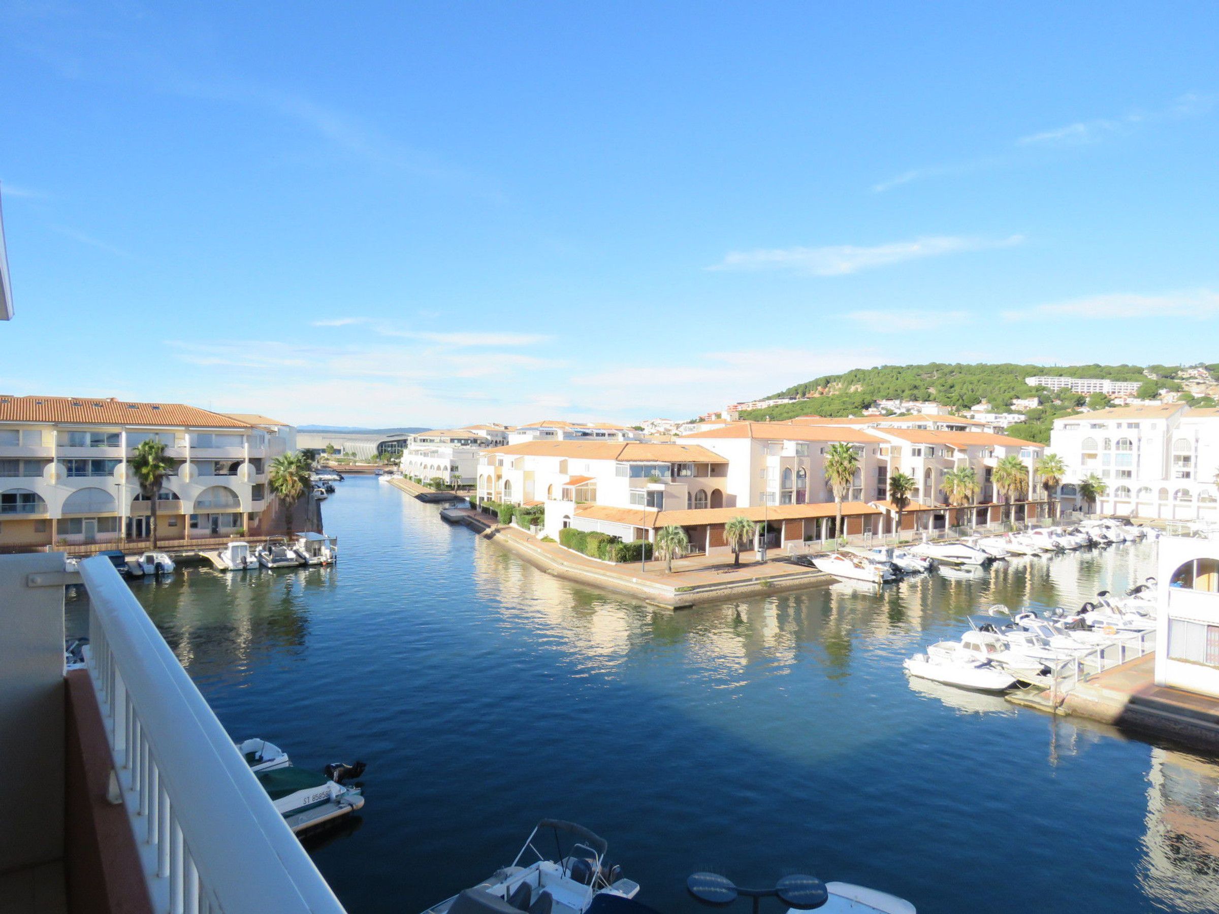 A marina with boats docked, buildings with balconies, and a clear sky.