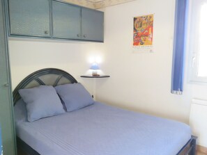 A bed with a headboard, a wall-mounted shelf with a lamp, and a poster on the wall.